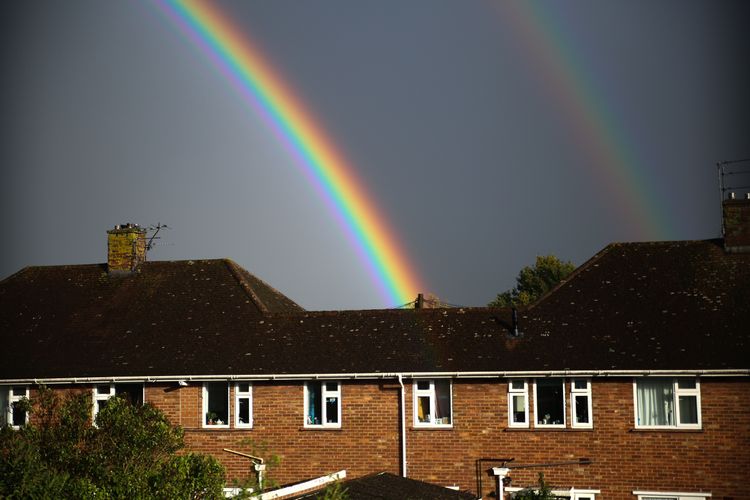 a terrace of houses with grey clouds, and a double rainbow. Photo by Victoria Feliniak on Unsplash